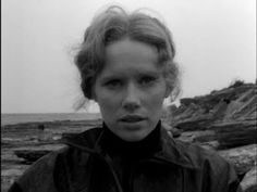 a black and white photo of a woman standing on rocks near the ocean with her hair blowing in the wind