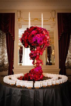 a table topped with lots of red flowers and place cards in front of a window