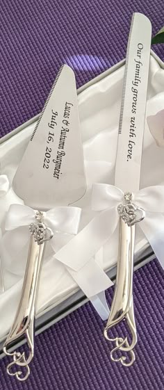 two silver spoons sitting on top of a white box with ribbon around them and tags attached to the handles