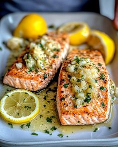 two salmon fillets on a white plate with lemons and garlic garnish