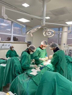 doctors in green scrubs perform surgery on an operating room floor with lights above them