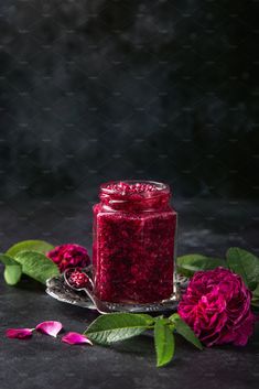 a glass jar filled with red liquid next to pink flowers on a black tablecloth