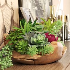 a wooden bowl filled with green plants on top of a table next to framed pictures