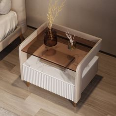 a white table with a glass top sitting on a wooden floor next to a bed