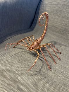 a wire crab sitting on top of a blue couch with its legs spread out and it's head turned to the side