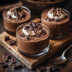 three desserts with chocolate and whipped cream in small glasses on a cutting board next to spoons