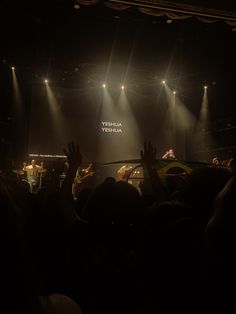 people are in the dark with their hands up and one person is standing on stage