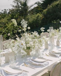 the table is set with white flowers in vases and place settings for dinner guests