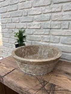 a stone bowl sitting on top of a wooden table next to a potted plant