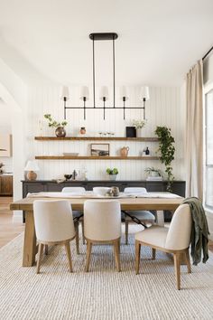 the dining room table is surrounded by white chairs and wooden shelves with plants on them