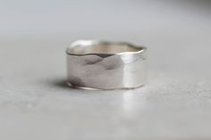 A chunky organic, rustic recycled silver ring with a hammered/textured finish. This unisex ring has an uneven finish and each one is truly unique. These make a lovely men's wedding band. The hammered finish gives the edge of the ring a 'wobbly' look which adds to it's character. The size measures approximately 8-9mm width x 1.2mm thickness. If you cannot see your size available then please get in touch as these rings can be made in any size. There is a thinner band version of this ring available Male Rings Silver, Sterling Silver Rings Men, Masculine Silver Rings, Handmade Silver Brutalist Rings, Brutalist Hammered Silver Ring, Brutalist Sterling Silver Rings With Oxidized Finish, Mens Silver Rings Handmade Jewelry1000.com, Thick Ring, Rustic Rings