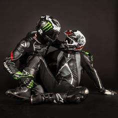 two motorcyclists are sitting on the ground in their racing suits and helmets