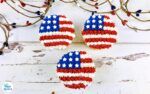 two american flags made out of yarn sitting on top of a white wooden table next to branches