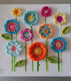 colorful crocheted flowers are displayed on a white surface with green stems and leaves