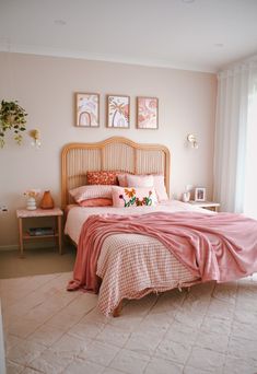 a bed with pink sheets and pillows in a bedroom next to two pictures on the wall