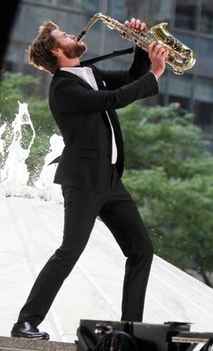 a man in a tuxedo playing a saxophone on the roof of a building