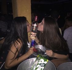 two women kissing each other while holding up bottles in front of their faces at a party