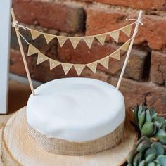 a white cake sitting on top of a wooden table next to a potted plant