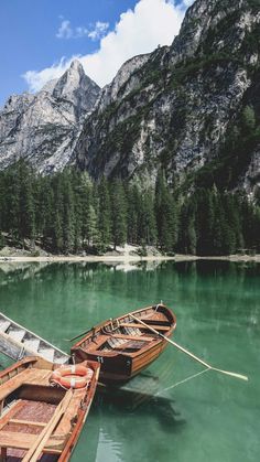 two wooden boats tied to the side of a mountain lake