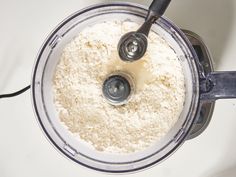 a food processor filled with white flour and two black spoons