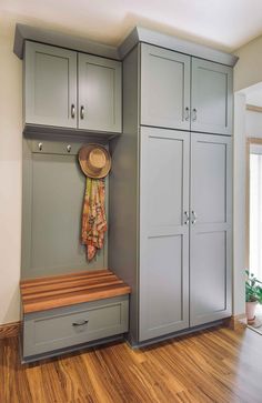 a room with gray cabinets and a wooden bench in the corner, next to a potted plant