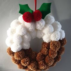 a christmas wreath hanging on the wall with pom - poms and holly leaves