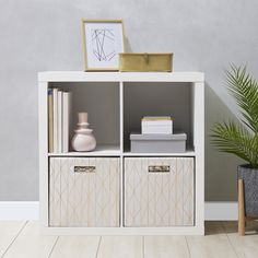 a white bookcase with two drawers and some books on it next to a potted plant