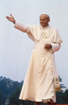 a man in a priest's outfit standing on top of a wooden platform with his arms outstretched