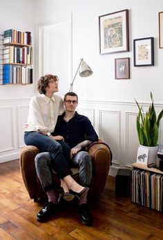 a man and woman sitting on a chair in front of a book shelf filled with books