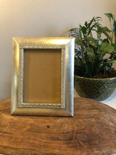 a small silver frame sitting on top of a wooden table next to a potted plant