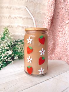 a glass jar with strawberries and daisies painted on the side, next to flowers