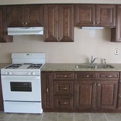 an empty kitchen with white appliances and brown cupboards on the wall above the stove