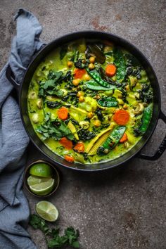 a pot filled with green vegetables and carrots on top of a gray surface next to lime wedges