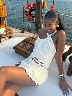 a beautiful young woman sitting on top of a white boat next to the ocean and smiling