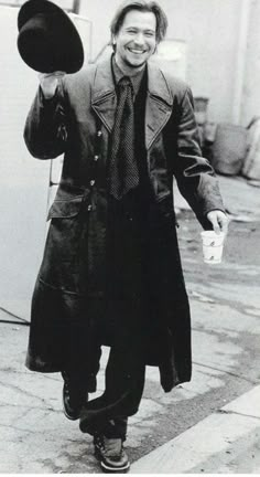 a man walking down the street with a hat on his head and holding something in his hand