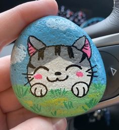 a hand holding a painted rock with a cat on it