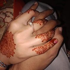 two hands with henna tattoos on them and one holding the other's hand