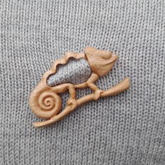 a wooden brooch depicting a chamelon sitting on a tree branch with its tail curled up