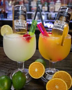 two glasses filled with drinks sitting on top of a table next to limes and orange slices