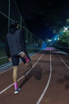 a man is running on a track at night with his leg in the air and wearing pink socks