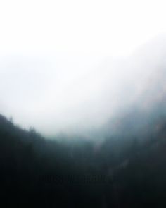 a blurry photo of mountains with trees in the foreground and fog on the ground