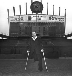 an old photo of a man with crutches in front of a scoreboard