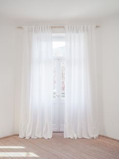 an empty room with white curtains and wooden floors