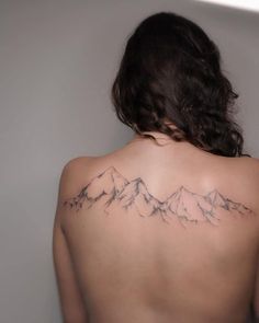 the back of a woman's shoulder with mountains tattooed on her left arm and chest