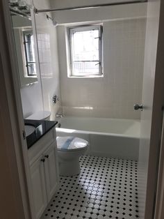 a white bathroom with black and white tile flooring on the shower wall, toilet and bathtub