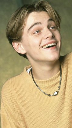 a young man smiling and wearing a yellow sweater