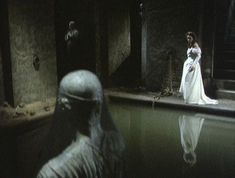 a woman in a white dress standing next to a man in a dark room with water