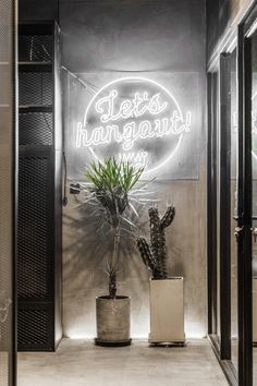 there is a neon sign that says lets hangout on the wall next to two potted plants