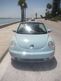 a blue car is parked on the side of the road next to the water and palm trees