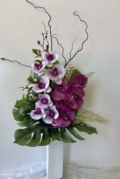 a white vase filled with purple flowers and greenery